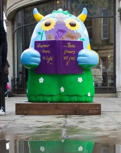 a green sculpture with horns and reading a purple book